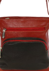 Rood en zwart leren crossbody tas met een gladde textuur, met twee ritszakken en contrasterende stiksels.