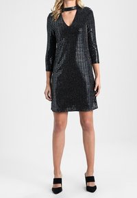 Svart paljettklänning med trekvartslånga ärmar, djup V-ringning och choker-detalj. Tyget har en strukturerad glans med horisontella randmönster.