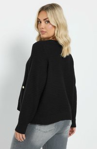 Svart stickad tröja med ett strukturerat mönster, rund halsringning och ribbade muddar. Har guldknappdetaljer på ärmarna.