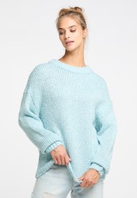 Világoskék kötött pulóver laza fazonnal, széles nyakkivágással és bordás mandzsettákkal. Texturált minta, puha, kissé bolyhos felülettel.