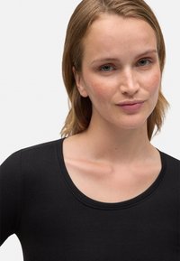 Top negro de manga larga con cuello redondo, confeccionado en una tela suave y elástica. La vista cercana resalta los contornos del cuello y los hombros.