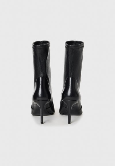 Zwarte leren high-heeled enkellaarsjes met een strak ontwerp, een gladde textuur en een taps toelopende stilettohak. Heeft minimale stiknaden.