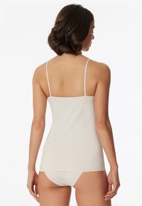 Light beige tank top with thin adjustable straps, made of smooth, stretchy fabric, featuring a simple, fitted design and no visible patterns.