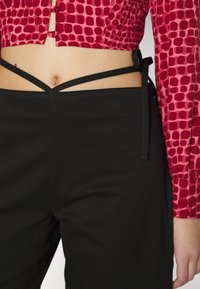 Top cropped com padrões em vermelho e rosa combinado com calças pretas de cintura alta com laços cruzados nas costas. Textura suave, design justo.
