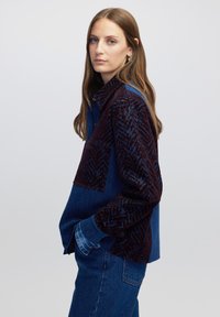 Spijkerblouse met een textuur in donkerrood afgesneden paneel met een geometrisch patroon, contrasterende blauwe mouwen en knoopmanchetten.