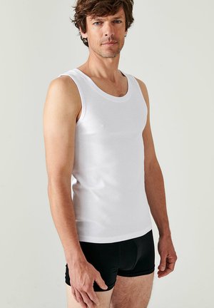 White cotton tank top with a rounded neckline, fitted design, and broad shoulder straps, paired with black fitted shorts.