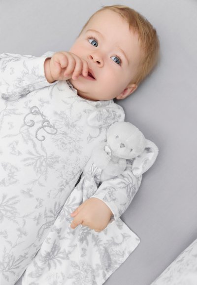 Hallikas lillemustriga kangast unisärk pikkade varrukatega; laps hoiab käes väikest halli pehmet mänguasja, millel on longus kõrvad. Pehme ja tekstuuriga välimus.