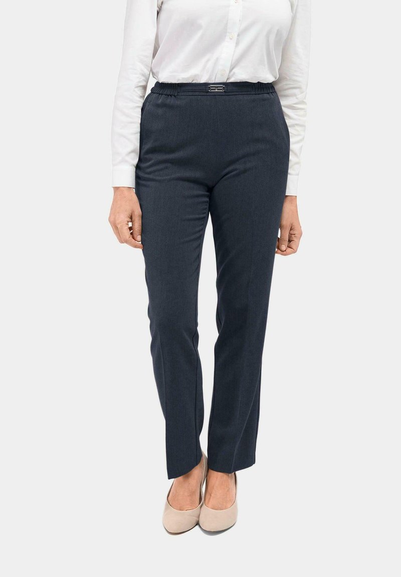 Donkerblauwe broek met een gladde textuur, elastische tailleband en subtiele glans. Gecombineerd met lichtbeige schoenen.