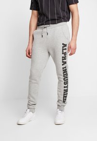 Grijze joggingbroek met een taps toelopende pasvorm, voorzien van een zijprint "ALPHA INDUSTRIES" in vet zwart. Gemaakt van zachte stof met een elastische tailleband.