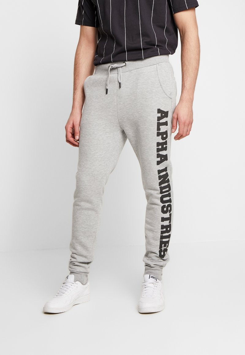 Grijze joggingbroek met een taps toelopende pasvorm, voorzien van een zijprint "ALPHA INDUSTRIES" in vet zwart. Gemaakt van zachte stof met een elastische tailleband.