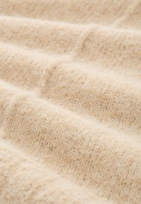 Beżowa dzianina o miękkiej, teksturowanej powierzchni, z delikatnymi poziomymi prążkami i puszystym wyglądem.