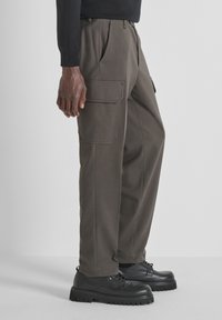 Pantaloni cargo di un verde oliva scuro, con due grandi tasche laterali, una vestibilità comoda e un tessuto liscio e testurizzato. Abbinati a scarpe nere.