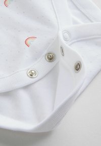 Bodysuit en coton blanc avec un petit motif à pois et une broderie arc-en-ciel ; présente des boutons-pression au bas et un col côtelé doux.