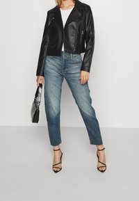 Černá kožená zkrácená bunda, bílý tričko, světlé rovné džíny, černé páskové lodičky, držící texturovanou černou kabelku.