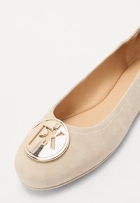 Ballerines en suède beige avec un bout arrondi, ornées d'un accent circulaire doré bien en vue à l'avant. Doublure intérieure lisse.