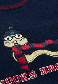 Maglione blu navy con un personaggio dei cartoni animati ricamato in rilievo che indossa un cappello blu, una sciarpa a righe rosse e blu e dettagli color crema.