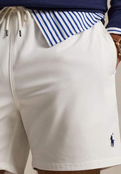 Λευκά σορτς με κορδόνι και σήμα polo παίκτη με κέντημα σε ναυτικό μπλε, φορεμένα με μπλε-λευκό ριγωτό πουκάμισο και πουλόβερ σε ναυτικό μπλε χρώμα.