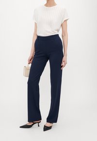 Marintröjor med skräddarsydd passform, subtil glans och sidofickor. I kombination med en strukturerad vit topp och svarta spetsiga klackar.