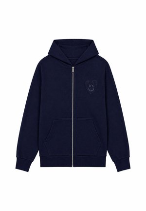 Sudadera azul marino con cremallera, bolsillos delanteros y un pequeño corazón bordado con ojos tachados y una sonrisa en el pecho izquierdo.