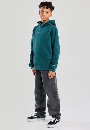 Felpa teal con tasca a marsupio, polsini a costine e un piccolo logo. Indossata con jeans grigi e sneakers bianco e nero.
