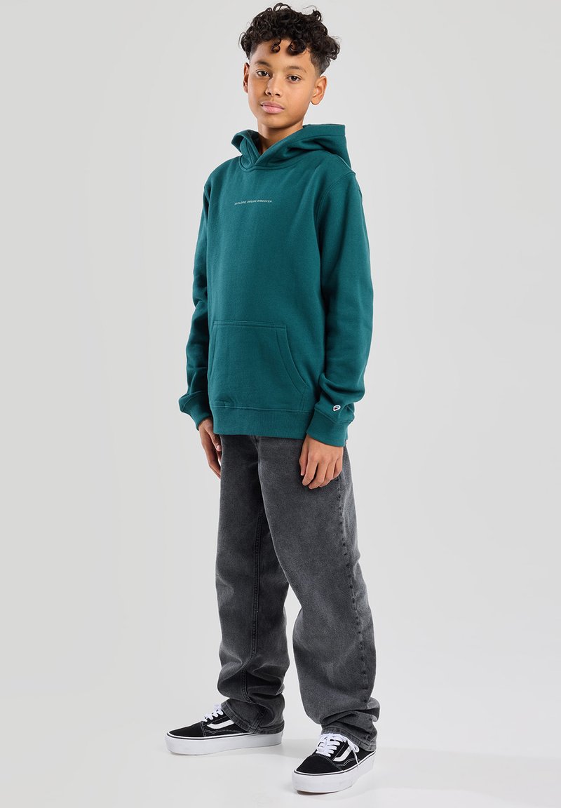 Teal huppari, jossa on kengurupussi, taitettu hihansuu ja pieni logo. Yhdistetty harmaisiin farkkuihin ja musta-valkoisiin lenkkareihin.