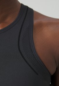 Camiseta deportiva negra sin mangas con un panel de malla texturizado y costuras elegantes a lo largo del escote y los hombros, destacando un diseño ergonómico.