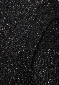 Vêtement en tricot noir avec un tissage lâche, présentant des fils brillants et texturés. Affiche un mélange de motifs de fil épais et fin.