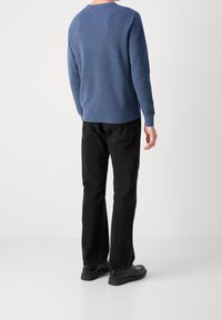 Maglione blu a maglia con tessuto texturizzato, collo rotondo e polsini a coste, abbinato a jeans neri a gamba dritta e scarpe nere.