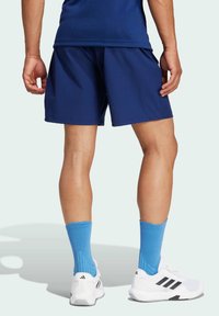 Navy shorts i ett lättviktigt material, med sidofickor och en lös passform, i kombination med blåa strumpor och vita sportskor med svarta detaljer.