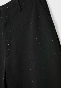 Mustat housut, jotka on valmistettu sileästä kankaasta ja joissa on hienovarainen kuvio pienistä hopeisista pilkuista. Sivutaskut ja räätälöity malli, joka antaa istuvan ilmeen.