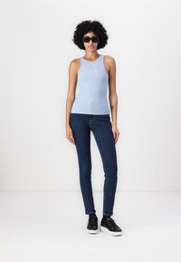 Hellblaues, geripptes Tanktop mit enganliegender Passform und einem kleinen Logodetail auf der Brust, kombiniert mit dunkelblauen Skinny Jeans und schwarzen Sneakers.