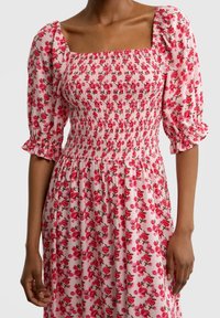 Vaaleanpunainen kukkamekko, jossa on neliönmuotoinen pääntie, rypytetty vartalo ja puffihihat. Kangas on kevyttä ja siinä on herkkä ruusukuosi.