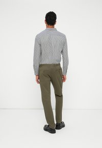 Men's casual outfit featuring a striped button-up shirt and olive green pants, with black shoes and visible back pocket details.