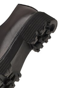 Botín de cuero negro hasta el tobillo con suela de goma robusta que presenta picos de tracción pronunciados. Detalle de cremallera en el lateral, diseño minimalista.