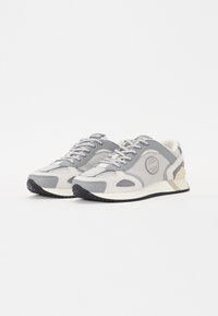 Sneaker sportive grigie realizzate con una combinazione di materiali in rete e suede, caratterizzate da una suola testurizzata e un design a punta arrotondata.