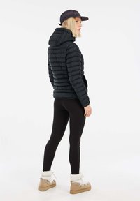 Zwarte pufferjack met capuchon, geribbelde muts, zwarte leggings en beige platformlaarzen met zachte witte stiksels. Kenmerkt zich door een aansluitend ontwerp.