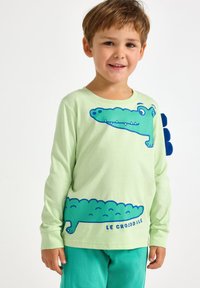 Zielona bawełniana koszula z długim rękawem z niebieskim graficznym nadrukiem krokodyla z przodu. Poniżej napis "LE CROCODILE". Miękka tkanina, swobodny krój.