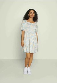 Vestido de padrão floral em cores pastel suaves, com decote quadrado, mangas bufantes e saia rodada. Combinando com ténis brancos.