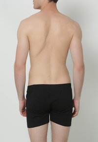 Zwarte katoenen boxershorts met een elastische tailleband, gezien van achteren. De stof ziet er glad en aansluitend uit.