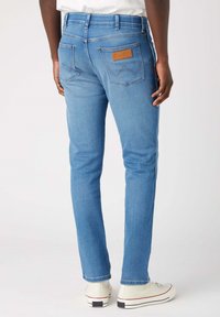 Jeans de mezclilla azul claro con un corte slim. Presentan un parche de cuero en el bolsillo trasero y sutiles acentos de costura. Diseño estándar de cinco bolsillos.