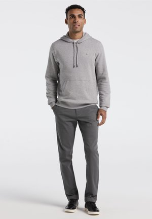 Hellgrauer Hoodie mit Kängurutasche, Kapuze mit Kordelzug und Logo. Kombiniert mit dunkelgrauen Hosen und schwarzen Sneakern. Glatte Textur überall.
