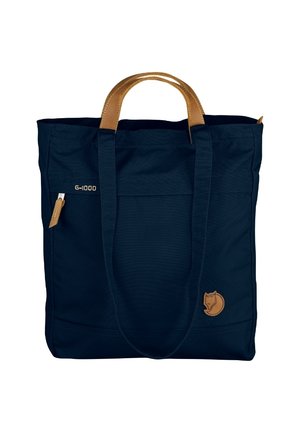 Marineblaue Tragetasche mit braunen Ledergriffen, Vordertasche mit Reißverschluss und kleinem Fuchs-Logo am unteren Eck.