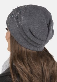 Căciulă tricotată gri, cu o textură ribbed, mărgele decorative și un design curbat, potrivită pentru vremea mai rece.