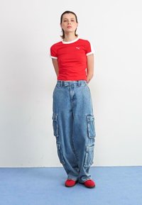 Red short-sleeve t-shirt with white trim, paired with loose blue denim cargo pants featuring side pockets, and red footwear.