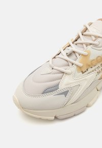 Lightweight sneaker in beige and gray tones, featuring a textured surface, mesh accents, and a cushioned sole with a distinct tread pattern.