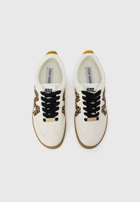 Adidași albi cu șireturi negre, părți laterale cu imprimeu leopard și tălpi din cauciuc. Prezintă accente aurii cu logo pe limba și panourile laterale.