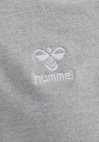 Tela gris con una superficie finamente texturizada. Logo bordado en forma de abeja y la palabra "hummel" en blanco, ubicado en el centro.