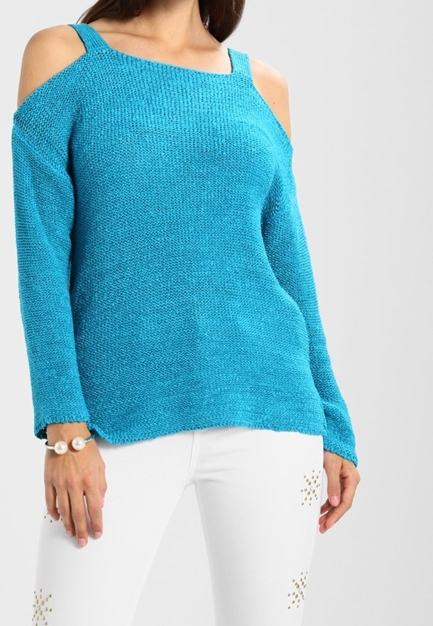Pull en tricot turquoise avec un design décolleté, des manches longues et une texture distinctive. Associé à un jean blanc avec des accents en clous.