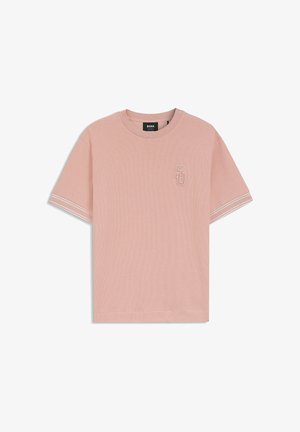 Camiseta de manga corta de color rosa claro con cuello redondo, con doble raya blanca en los puños de las mangas y un pequeño logo "SG" bordado en el pecho.