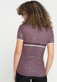 Bordeaux idrottstopp med korta ärmar, som har ett prickigt mönster, kontrasterande ränder över ryggen och textil med struktur.